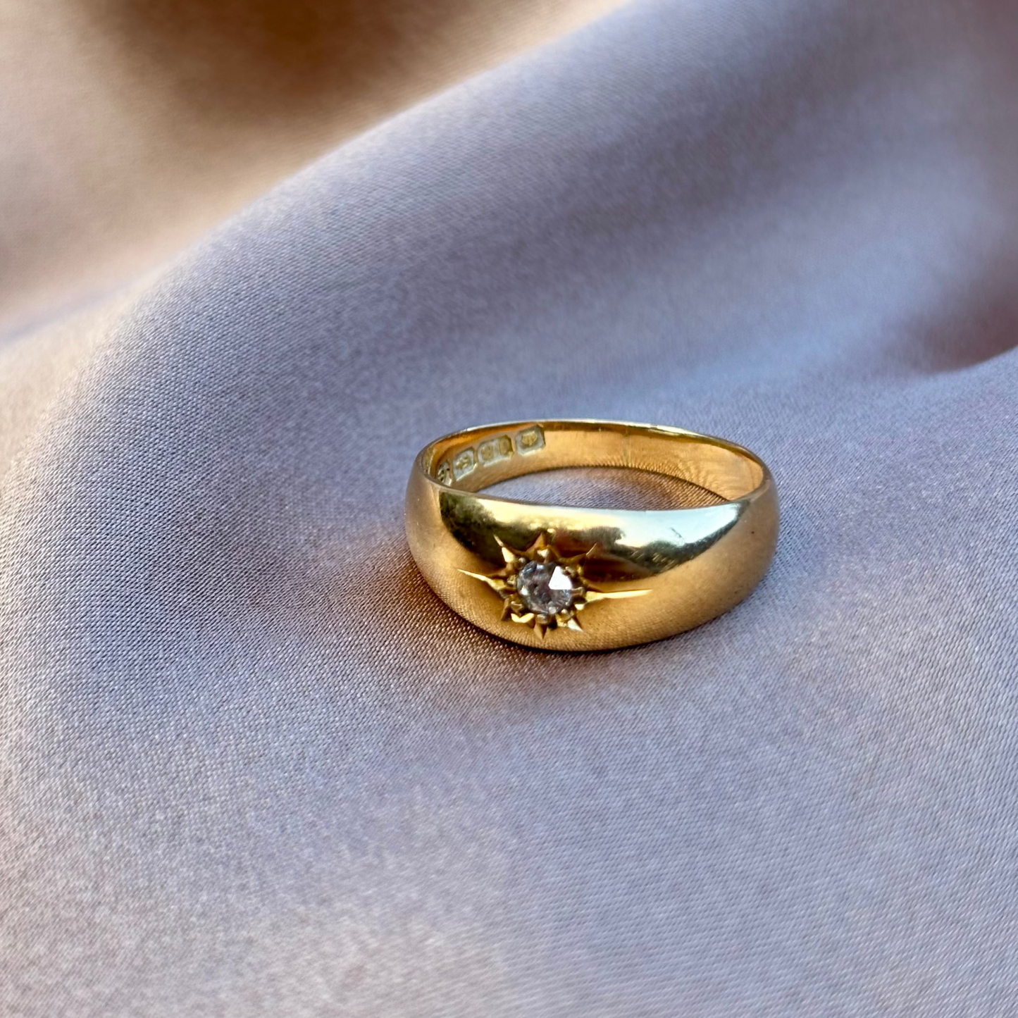 Gold gypsy ring with a diamond on a soft fabric background