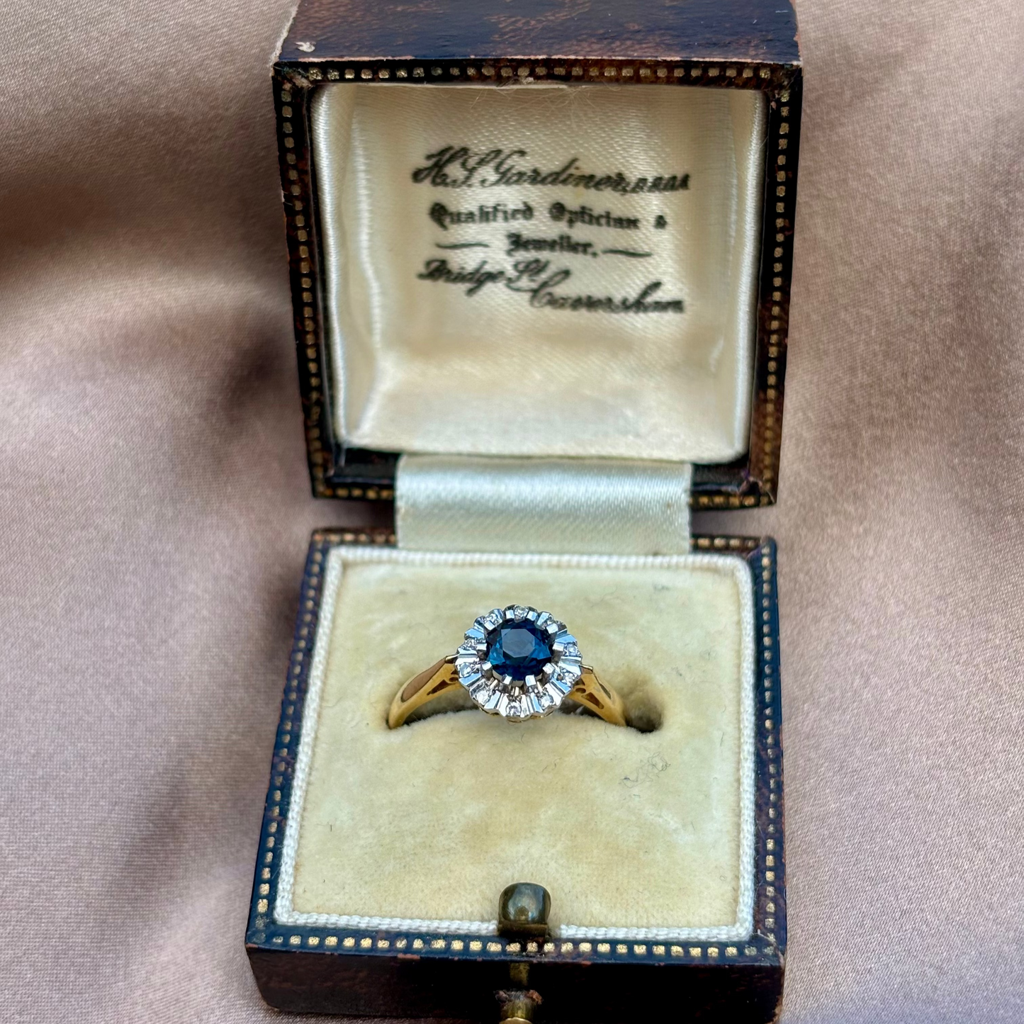 Gold ring with a blue sapphire in an open jewelry box on a beige background