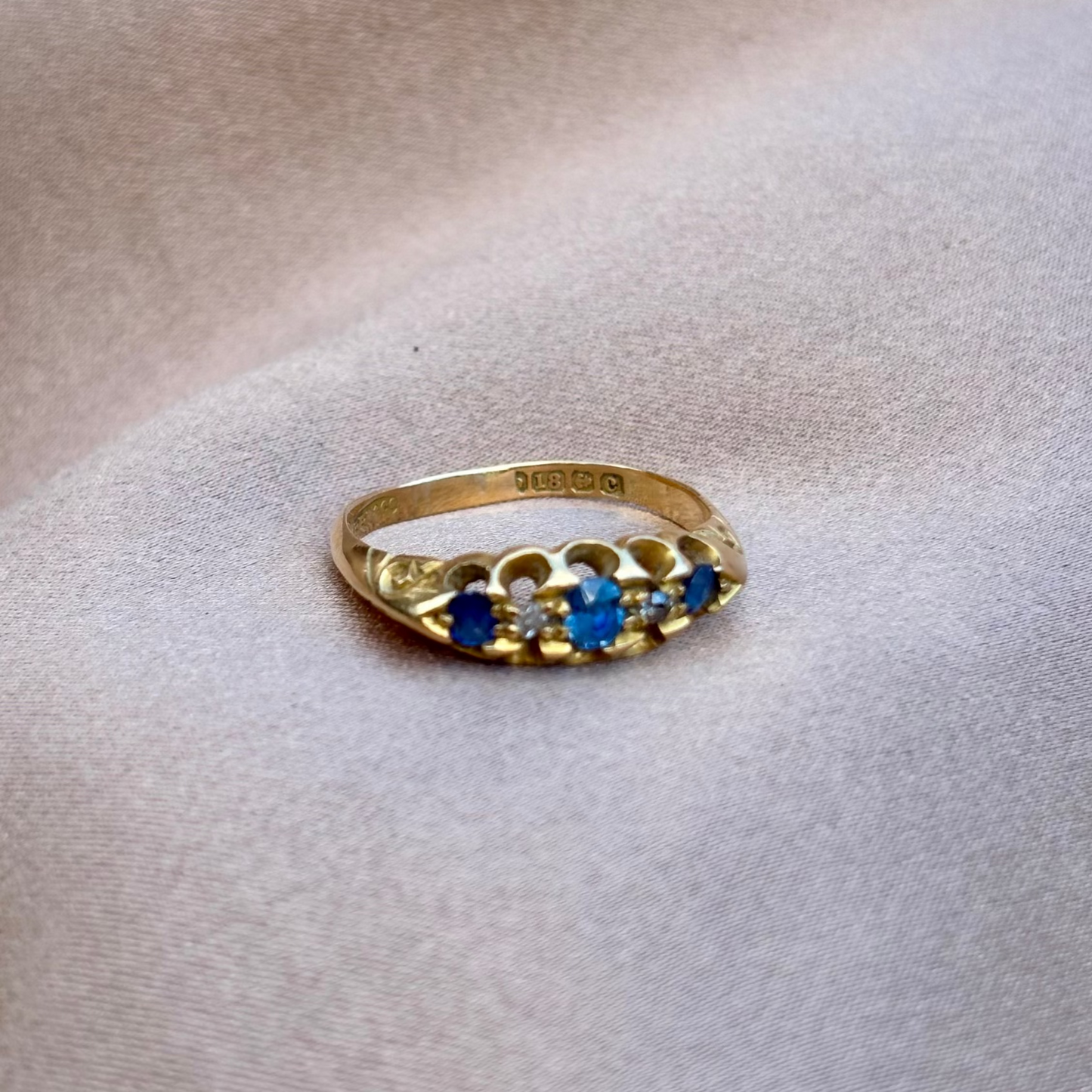 Gold ring with blue sapphires and diamonds on a beige fabric background