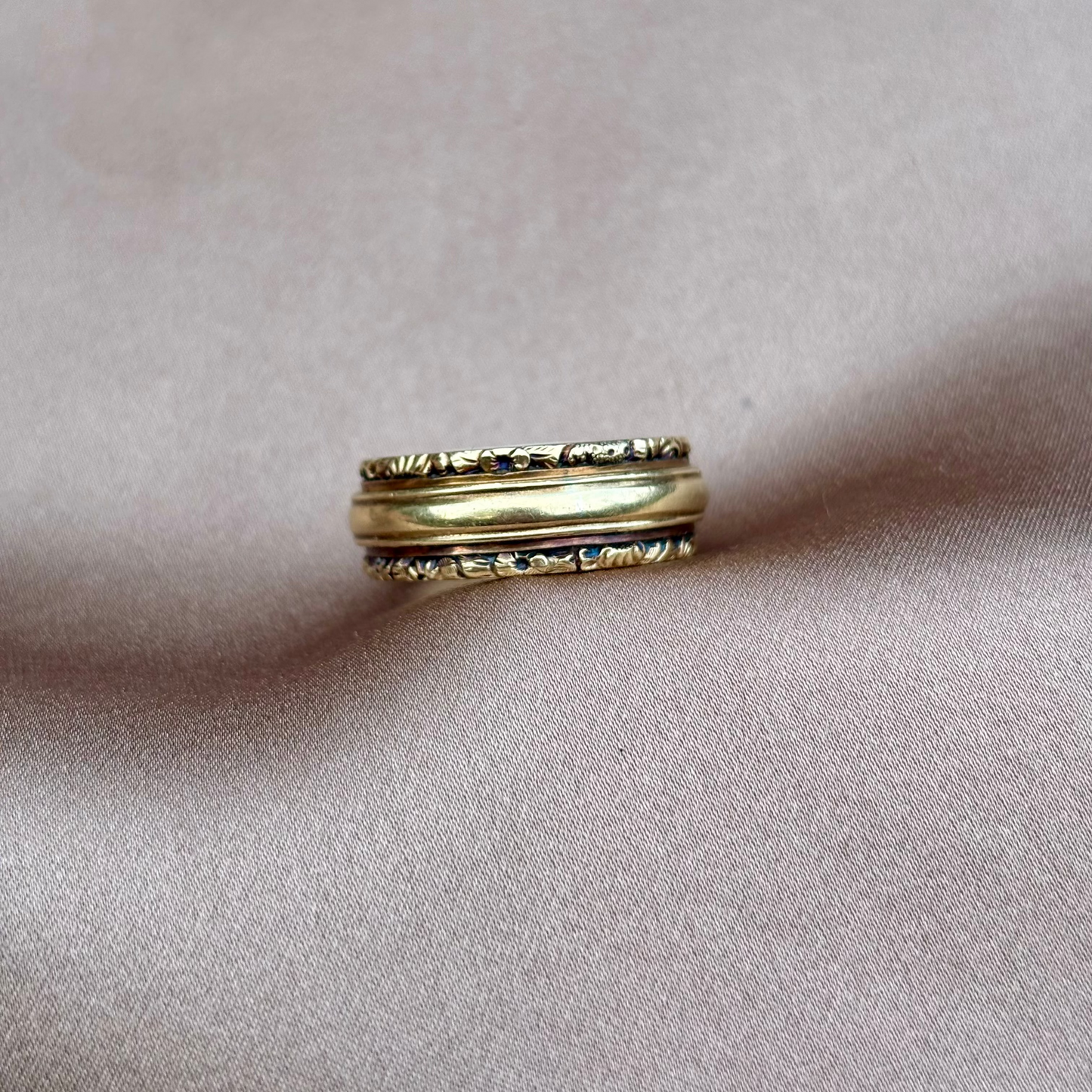 Gold ring with intricate design on a soft pink fabric background