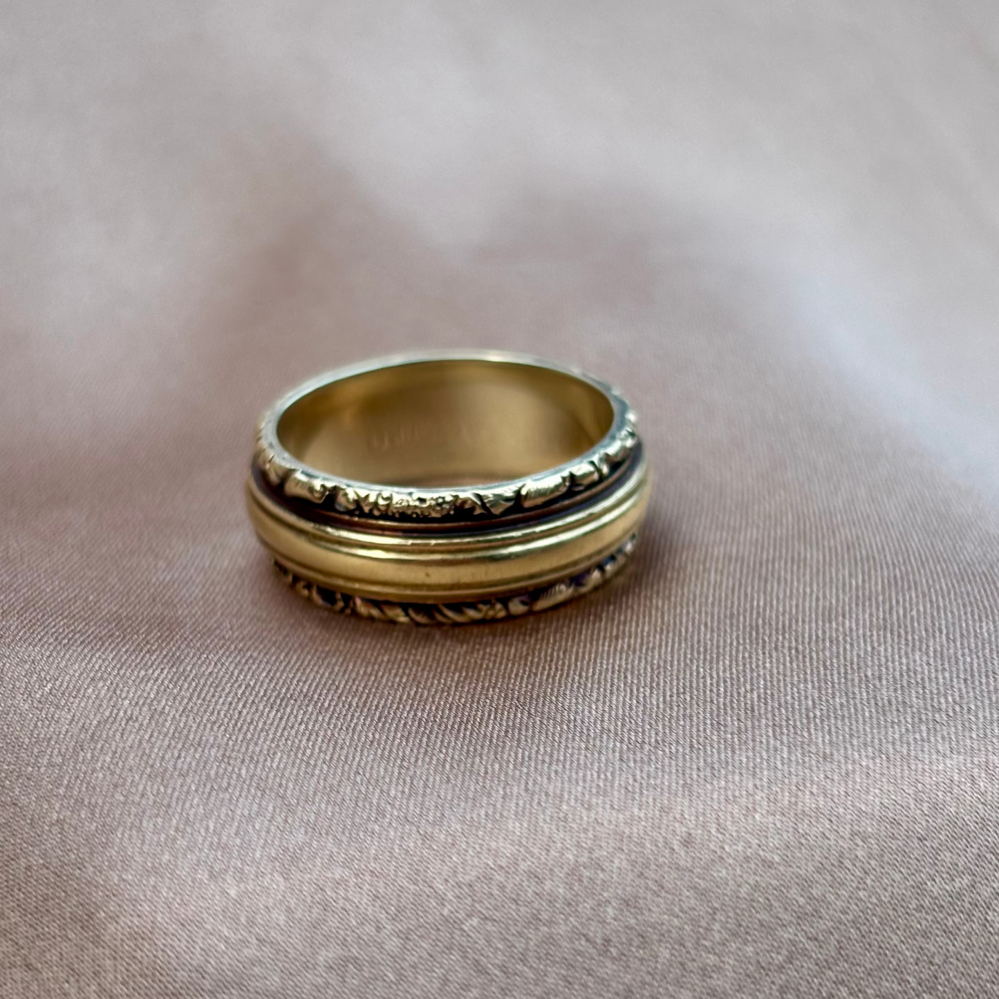 Gold ring with intricate design on a beige fabric background