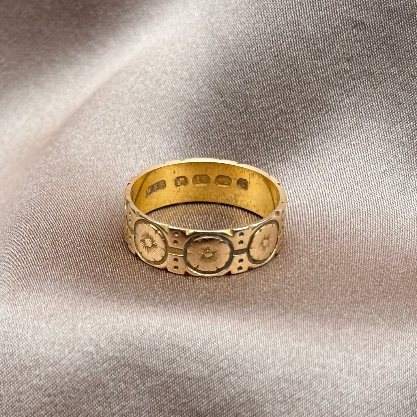Gold ring with intricate design on a textured beige surface