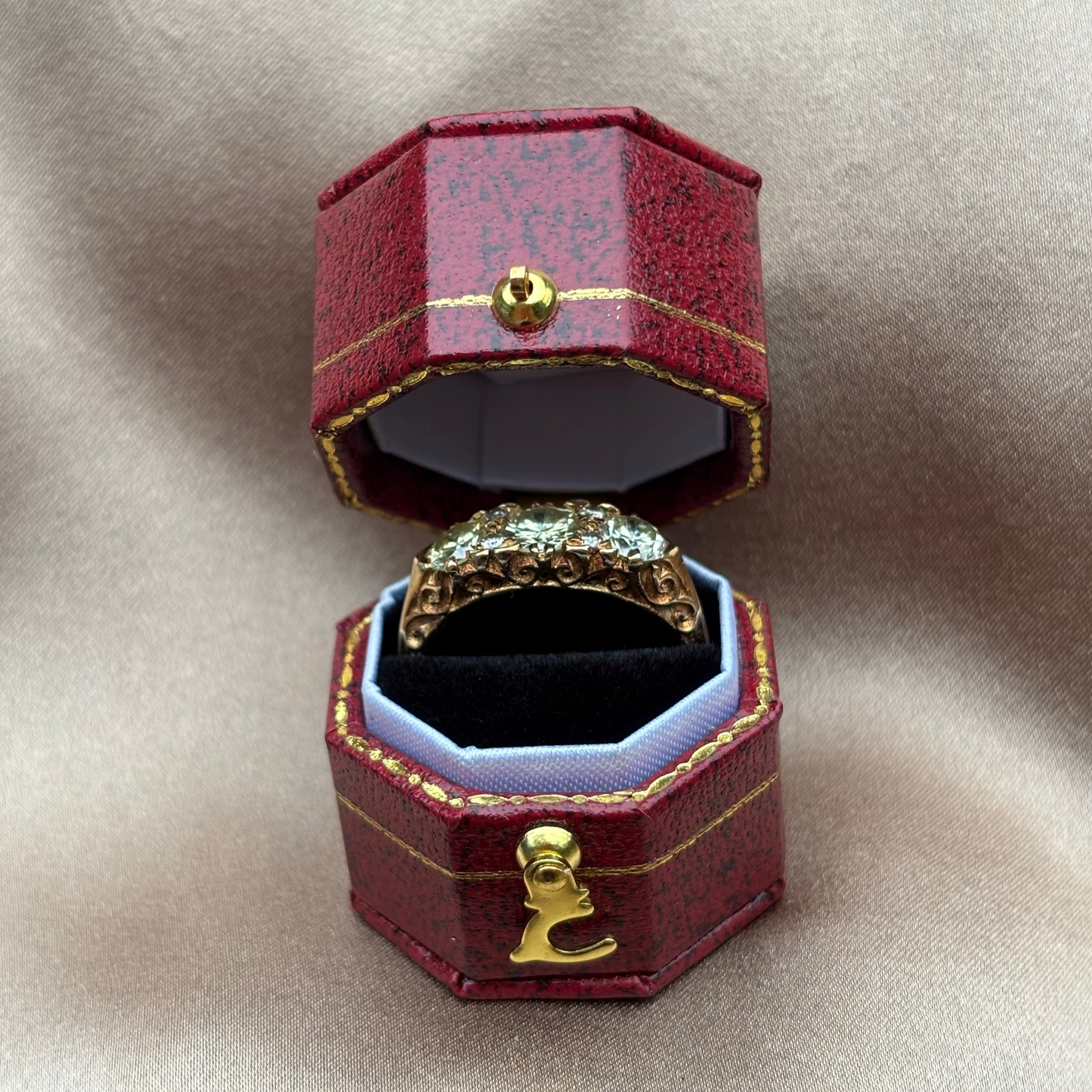 Gold ring in an open red jewelry box on a beige fabric background