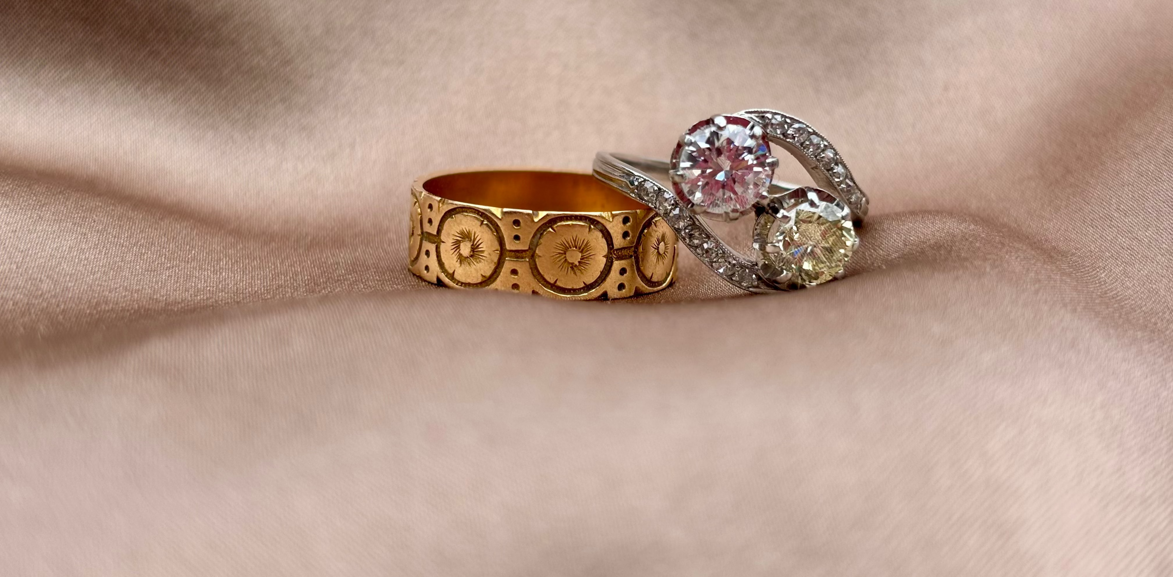 Two rings, one gold and one silver with a diamond, on a beige fabric background. posy ring and antique engagement ring