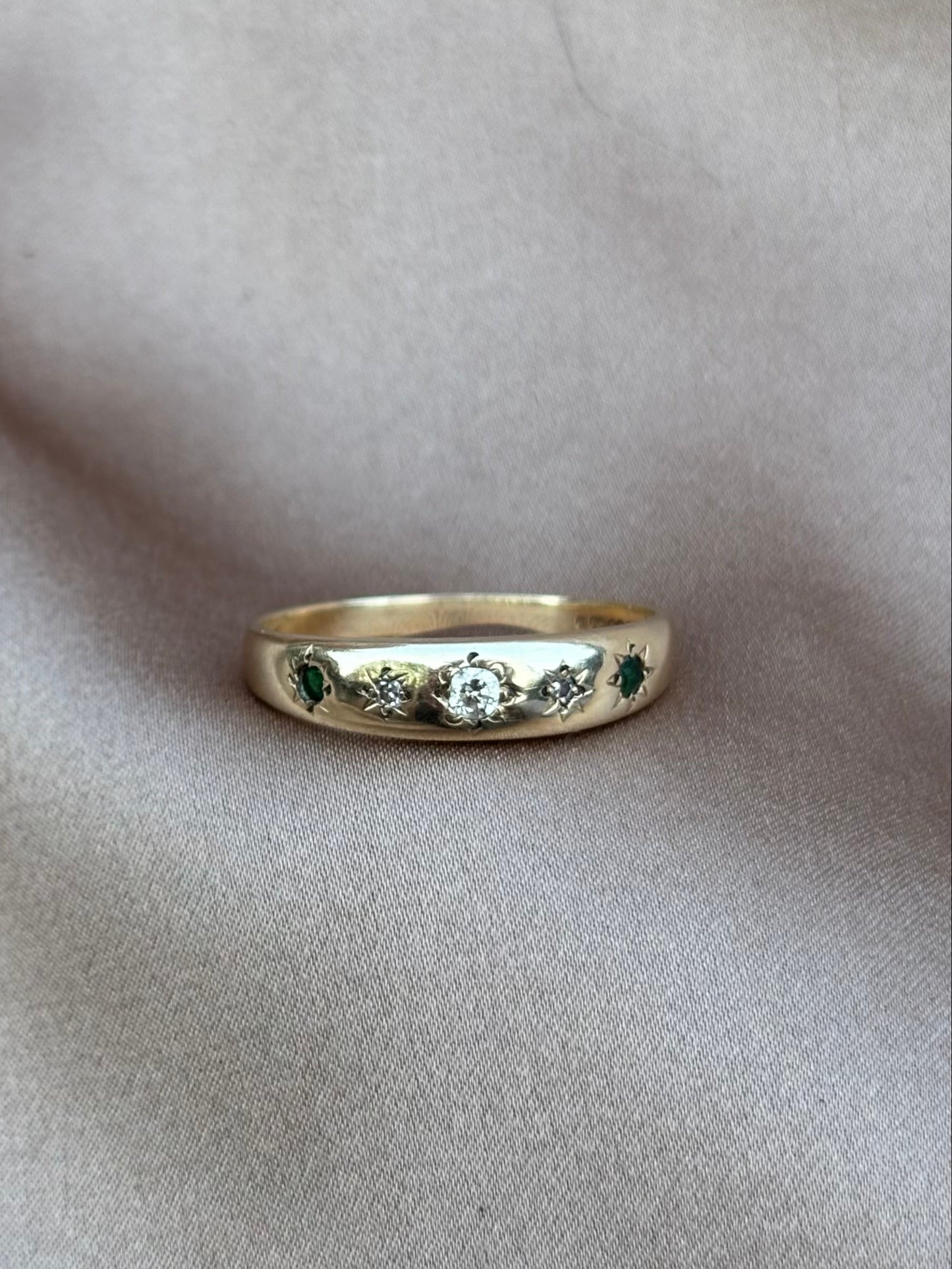 Gold ring with green gemstones on a beige fabric background