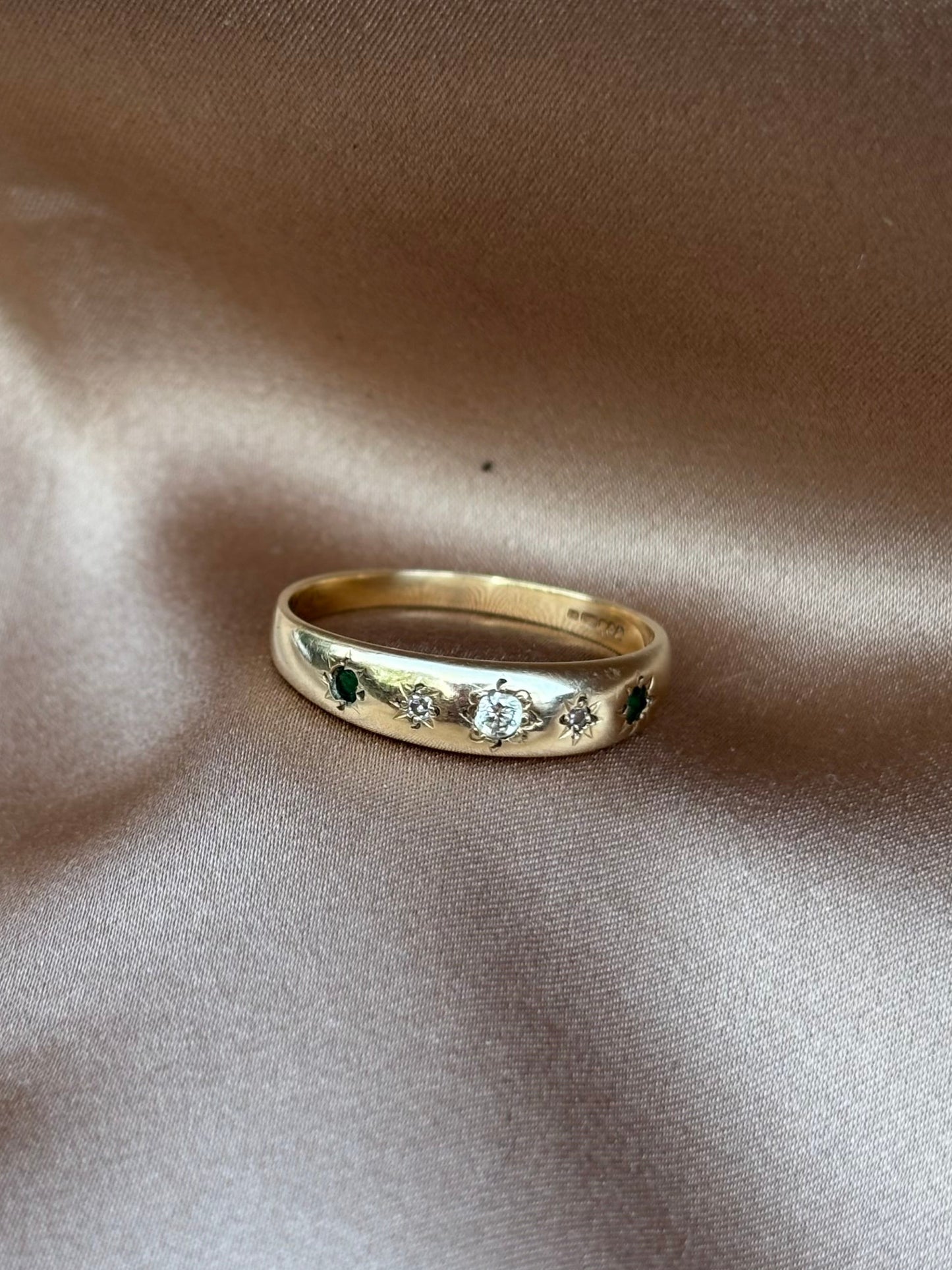 Gold ring with gemstones on a beige fabric background emerald and diamond