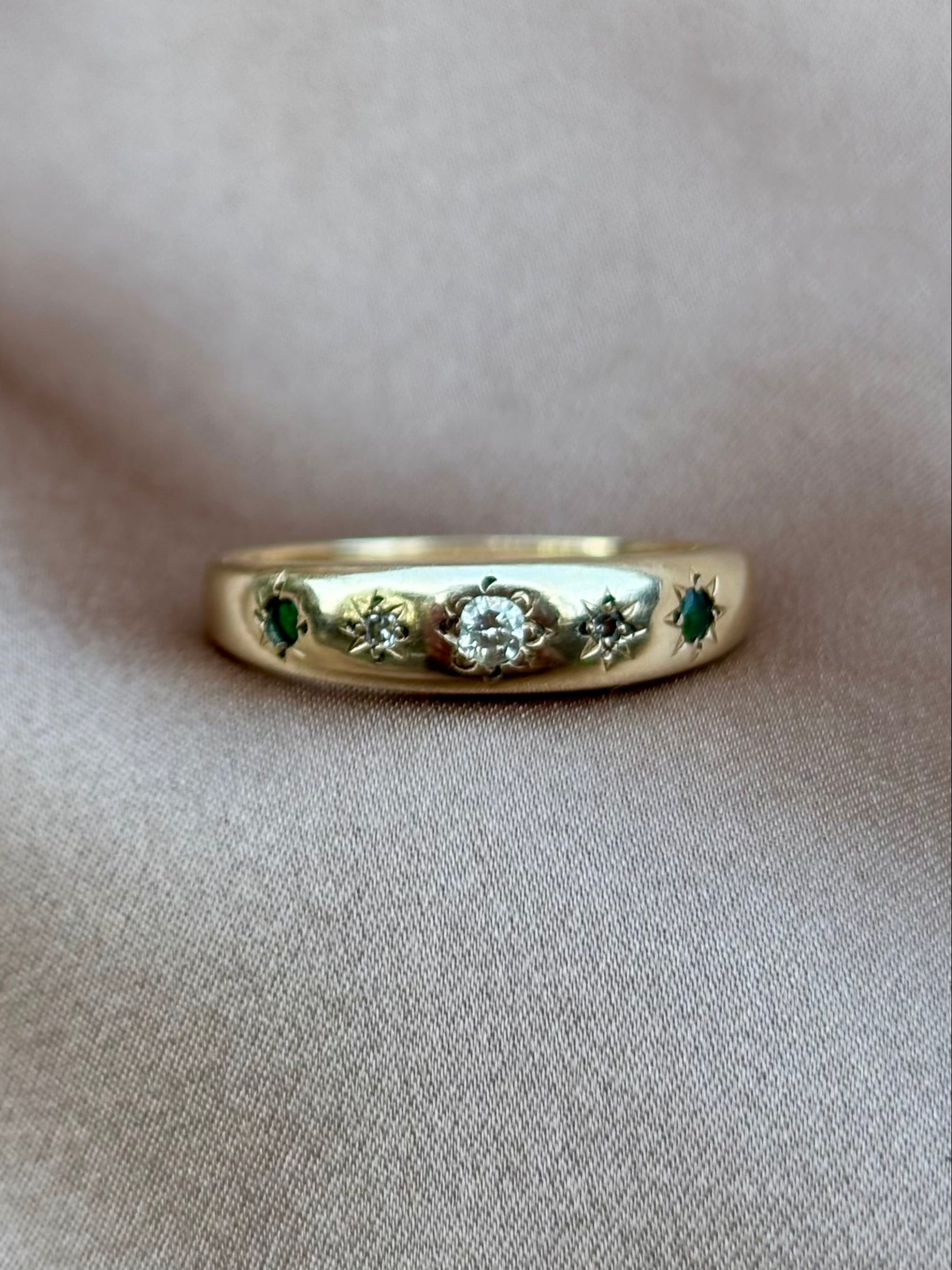 Gold ring with gemstones on a beige fabric background emerald and diamond