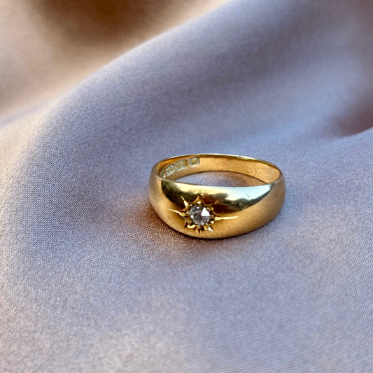 Gold gypsy ring with a diamond on a soft fabric background