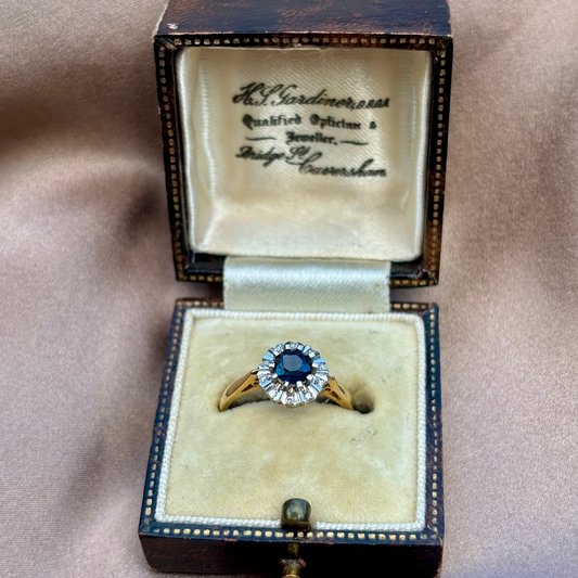 Gold ring with a blue sapphire  in an open jewelry box on a beige background