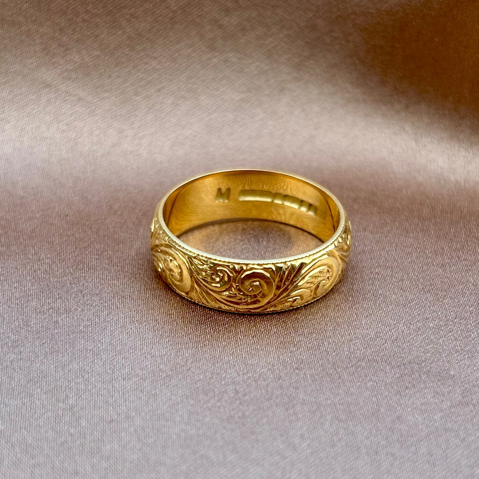 Gold ring with intricate designs on a beige fabric background