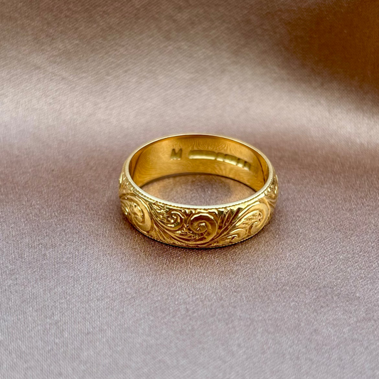 Gold ring with intricate designs on a beige fabric background