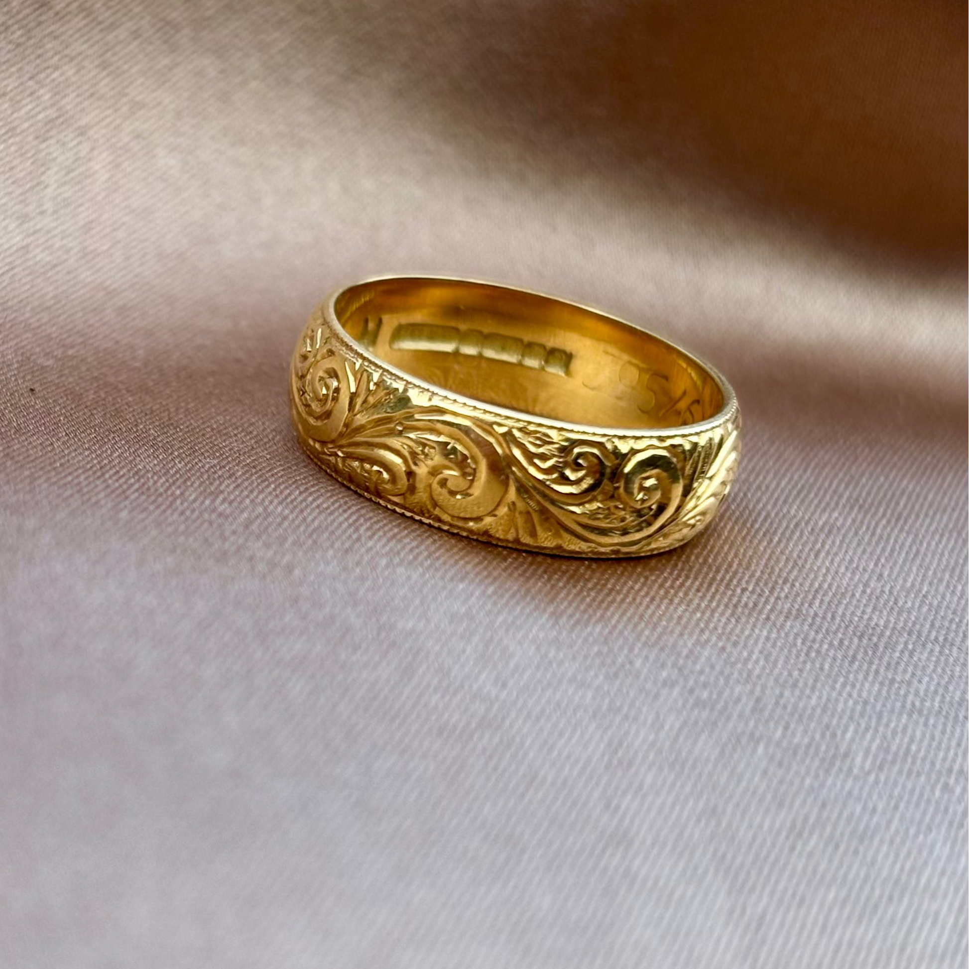 Gold ring with intricate design on a beige fabric background