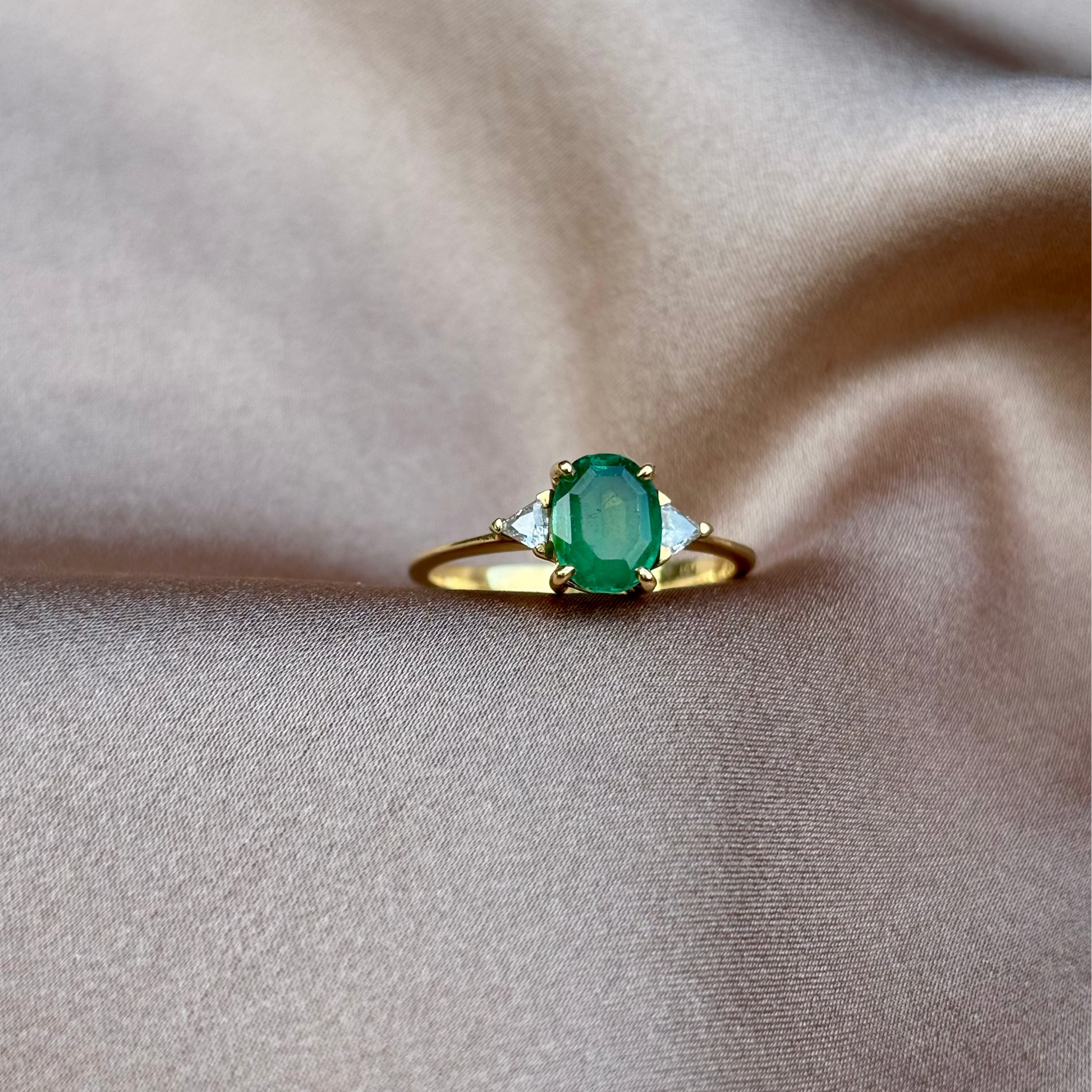 Gold ring with a green gemstone on beige fabric