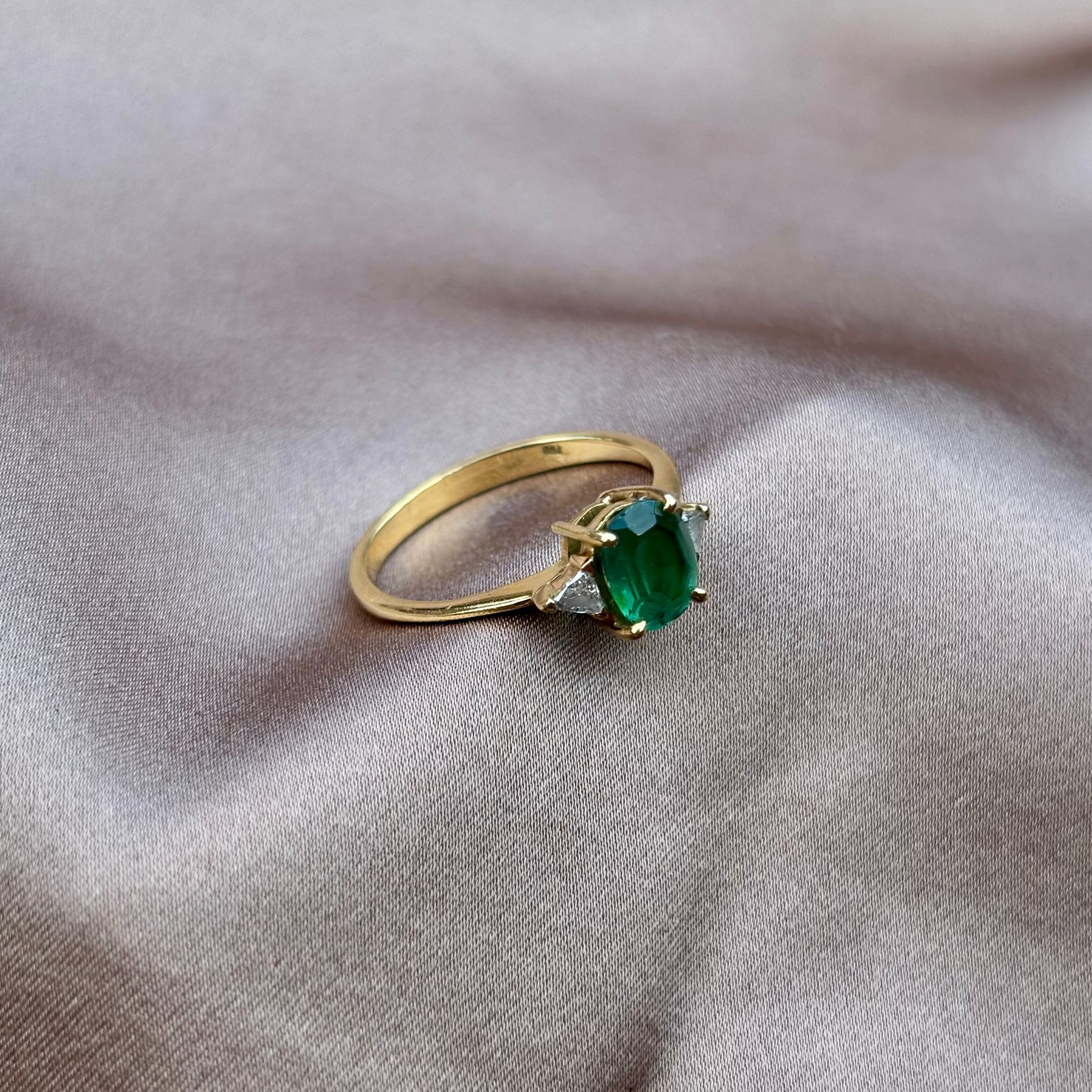 Gold ring with a green gemstone on a beige fabric background