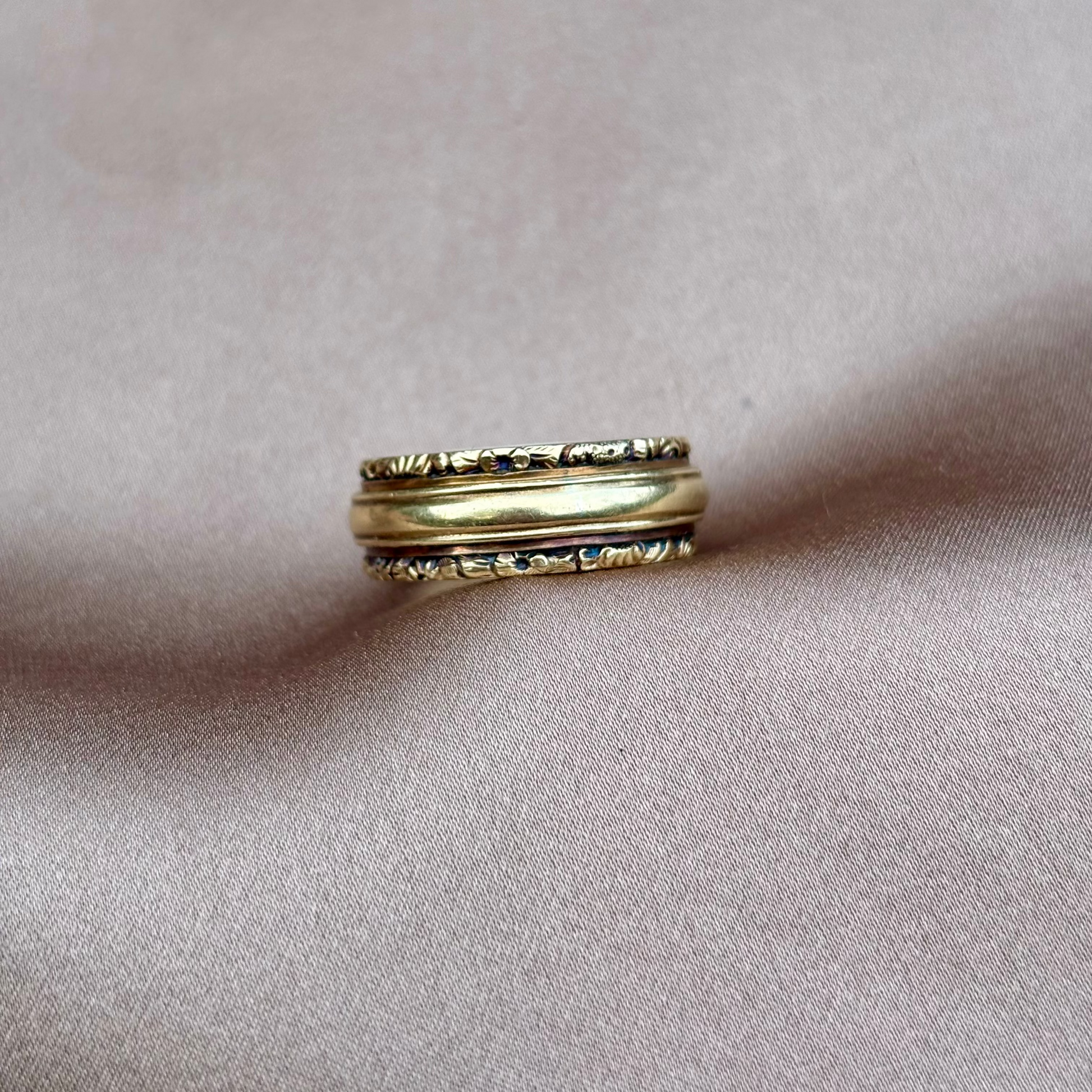 Gold ring with intricate design on a soft pink fabric background