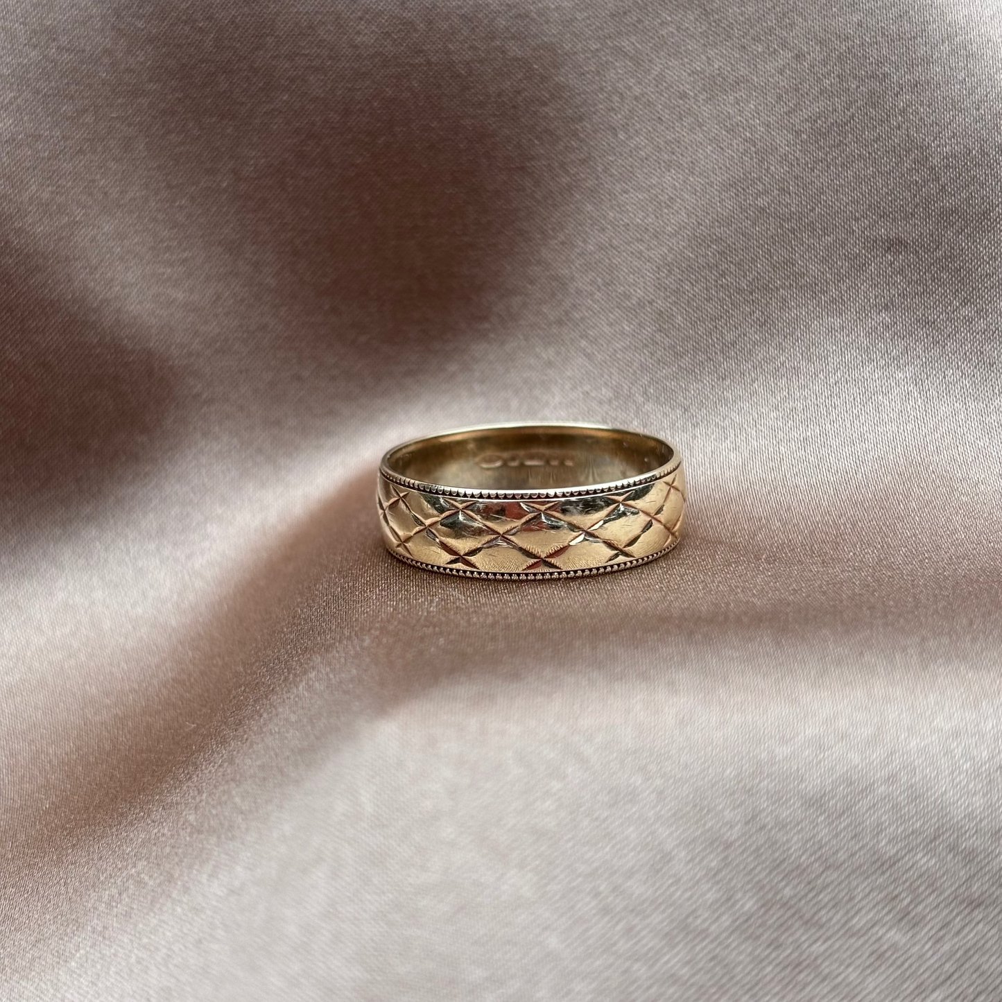 Gold ring with intricate design on a textured beige surface