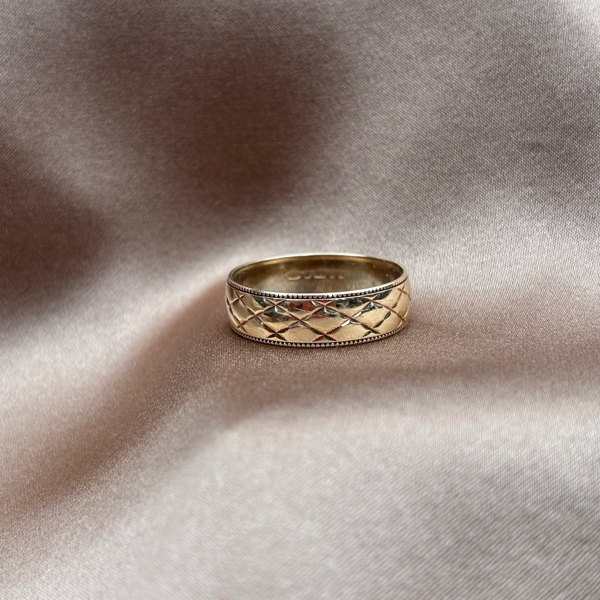 Gold ring with intricate design on a textured beige surface