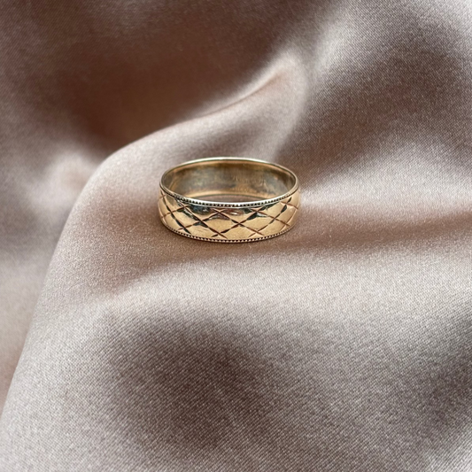 Gold ring with intricate design on a textured beige fabric background