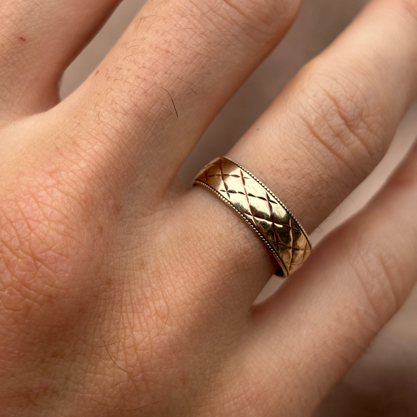 Gold ring with a textured band on a person's finger against a neutral background