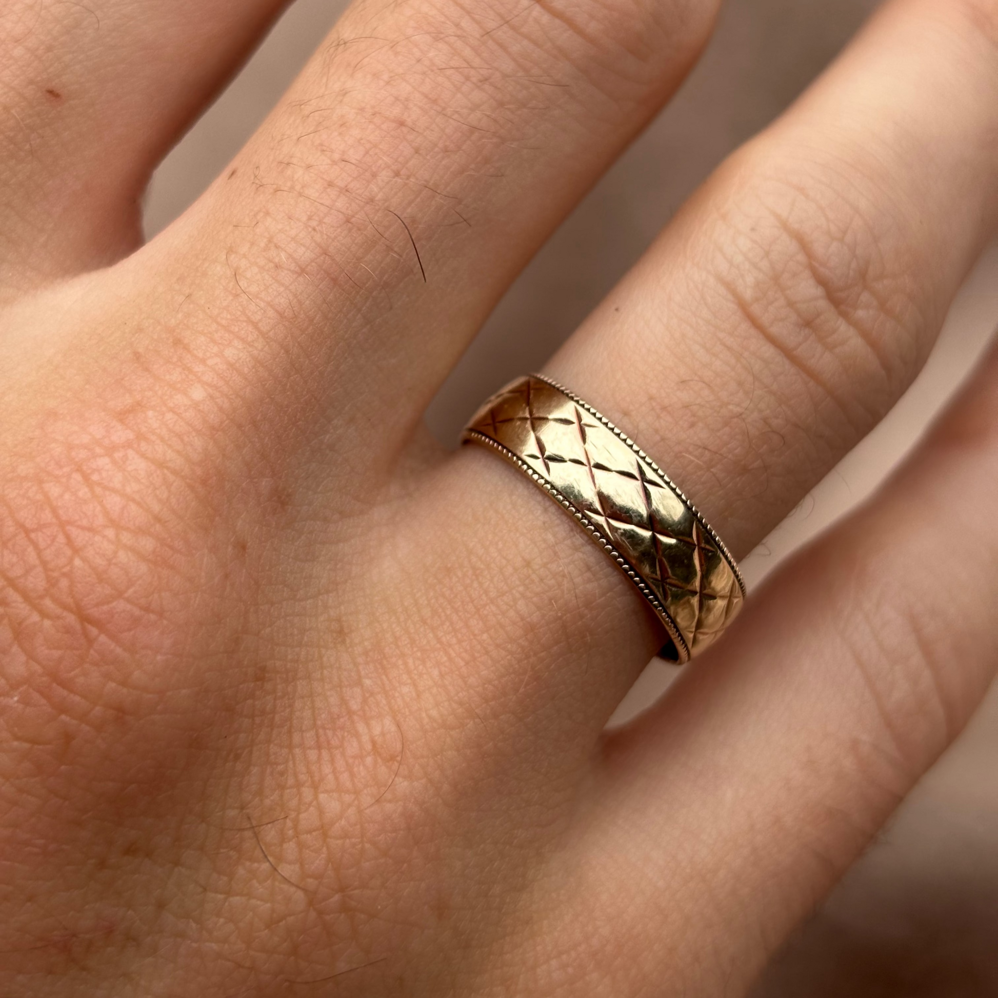 Gold ring with a textured band on a person's finger against a neutral background