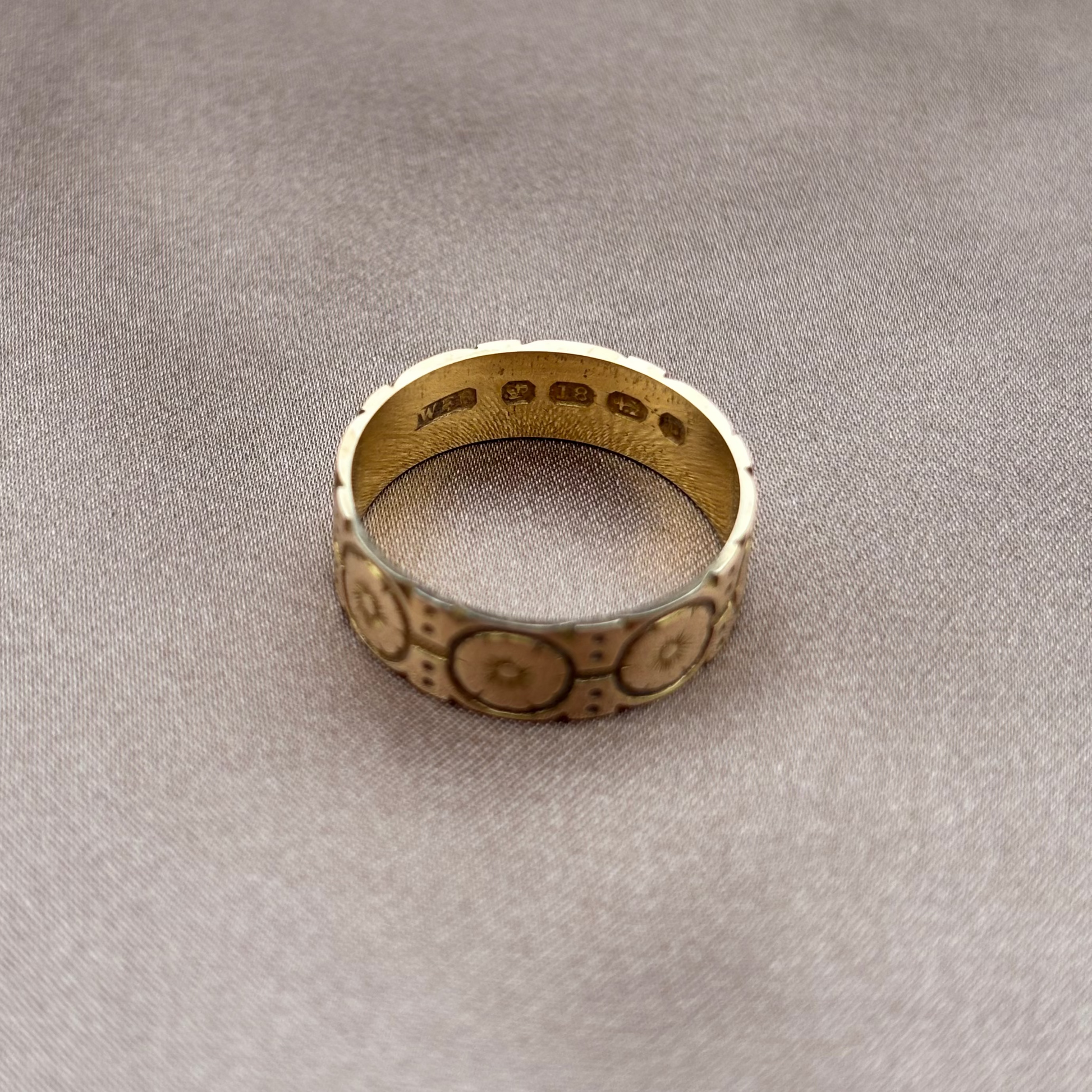 Gold ring with intricate designs on a beige fabric background