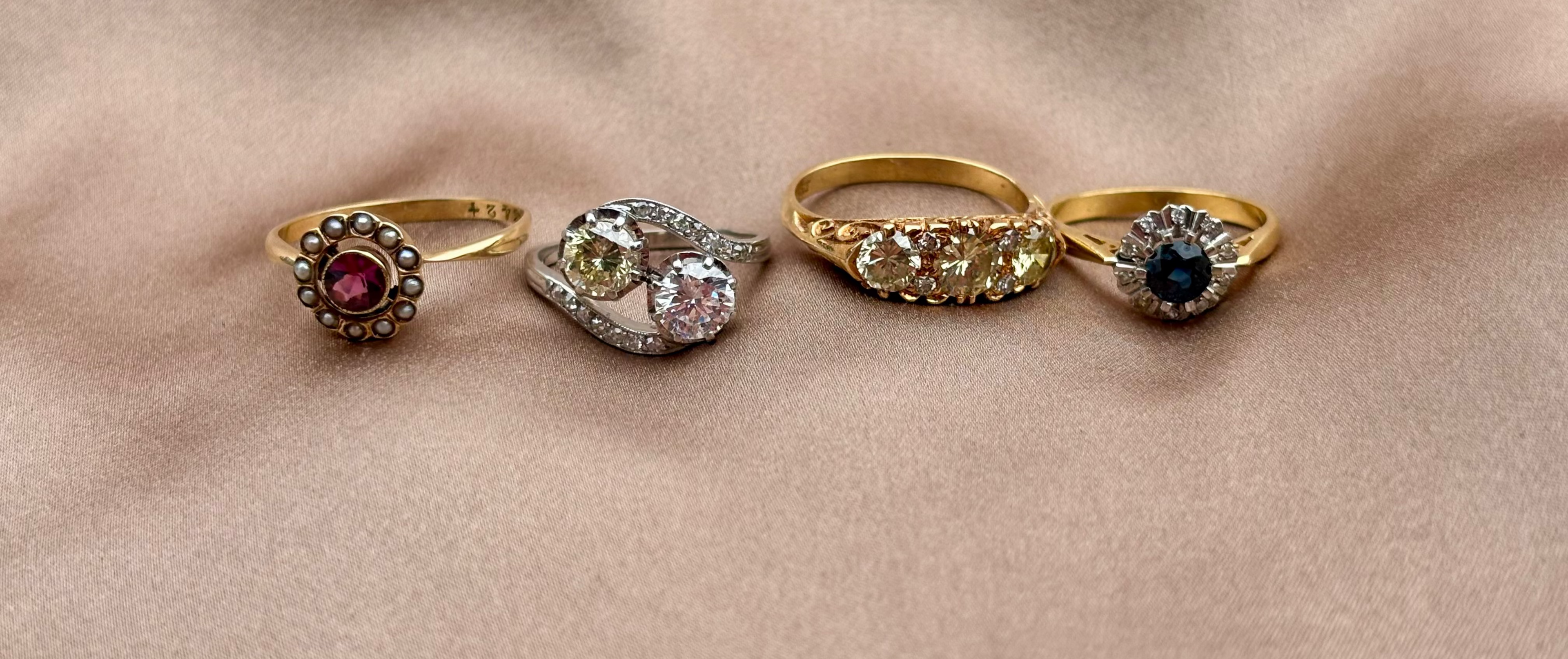 Four gold rings with gemstones on a beige fabric background diamond ruby and sapphire antique rings